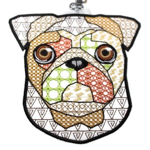 May include: A colourful embroidered pug face with brown eyes, a black nose, and a white background. The embroidery is done in a variety of geometric patterns, including triangles, squares and circles.