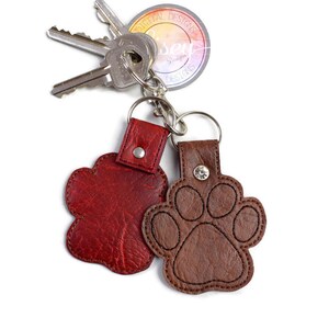 May include: Two leather paw print keyrings. One is red and the other is brown. Both have a silver ring and a silver button.