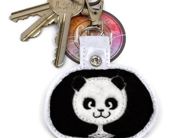 May include: White keychain with a black and white panda face embroidered on it. The keychain has a silver key ring and a silver clasp.