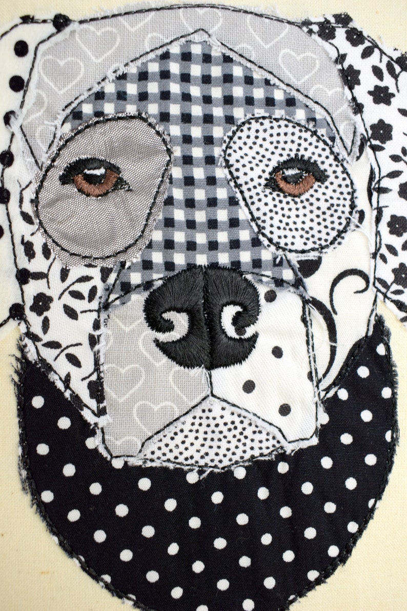 May include: A black and white patchwork fabric dog with a black nose and brown eyes. The dog is stitched onto a cream-colored background.