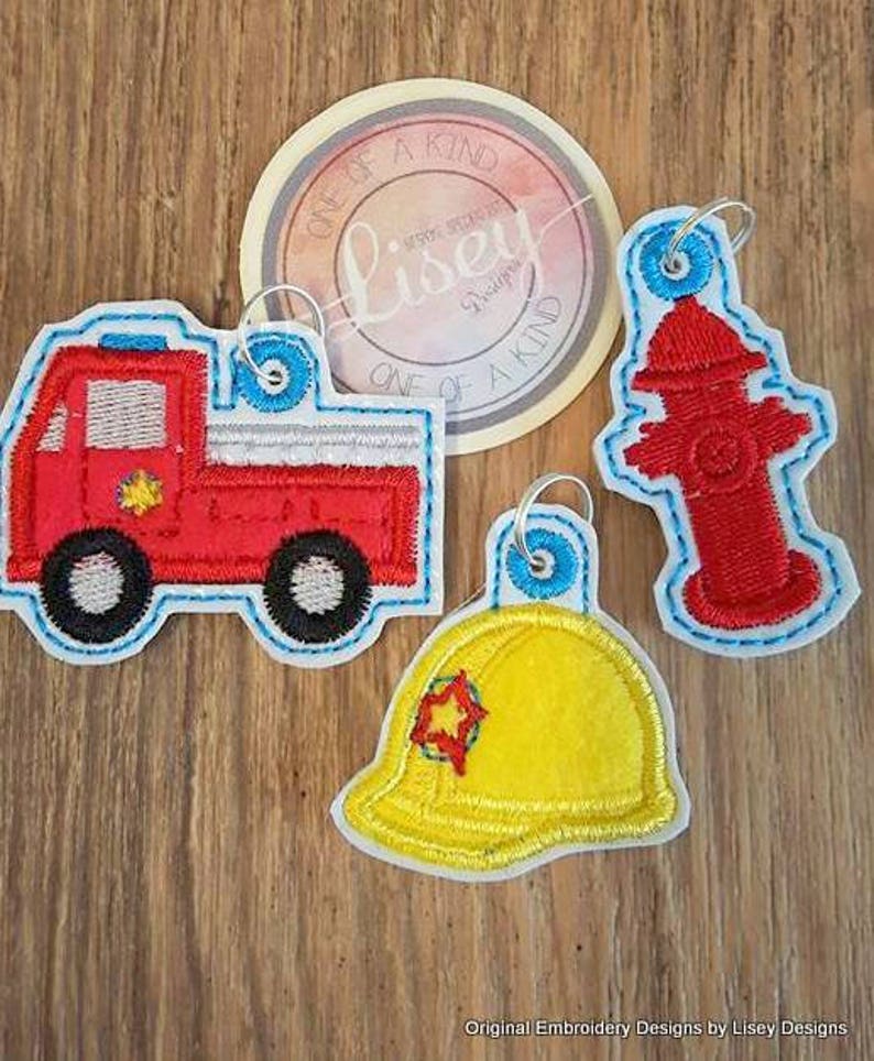 May include: Three embroidered patches featuring a red fire engine, a yellow firefighter helmet, and a red fire hydrant. The patches are all outlined in blue and have a white star in the centre.