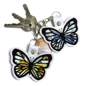 May include: Two butterfly-shaped keychains with floral patterns. One keychain is blue and white, the other is yellow and white. Both keychains have black outlines and are attached to silver key rings.