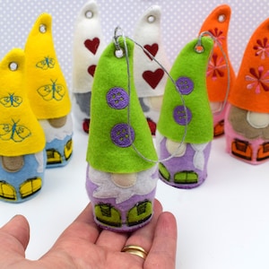 May include: A set of 6 felt gnome ornaments with different colored hats and embroidered details. The gnomes are wearing different colored hats with embroidered butterflies, hearts, and flowers.