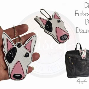 May include: White and black bull terrier dog face embroidery design for a 4x4 hoop. The design is shown on a white leather keychain and a black backpack.