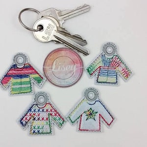 May include: Five colorful embroidered sweater keychains with a white background. The keychains are in different styles and colors, including red, green, blue, yellow, and white.