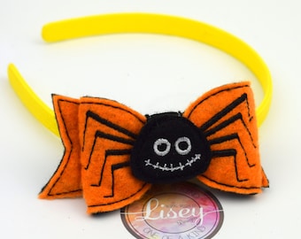 May include: A yellow headband with an orange and black felt spider bow. The spider has a stitched-on face with two eyes and a stitched-on mouth. The bow is attached to the headband with a knot. The headband is a one-of-a-kind design by Lisey Designs.
