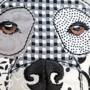 May include: Close-up of a dog's face made from patchwork fabric. The eyes are brown and the nose is black. The fabric is a mix of black and white patterns.