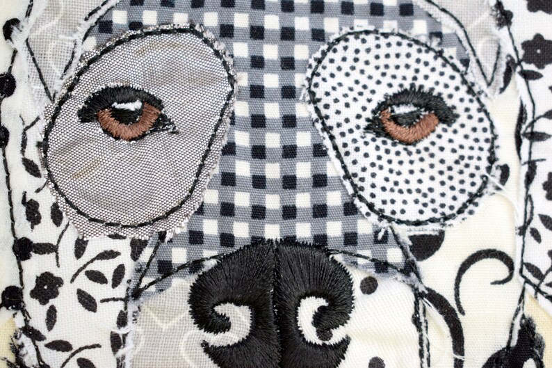 May include: Close-up of a dog's face made from patchwork fabric. The eyes are brown and the nose is black. The fabric is a mix of black and white patterns.