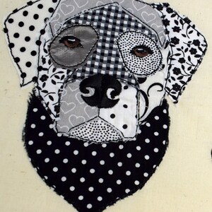 May include: Black and white patchwork fabric dog applique with a black and white polka dot bandana. The dog's eyes are brown and the fabric is sewn together in a variety of patterns.