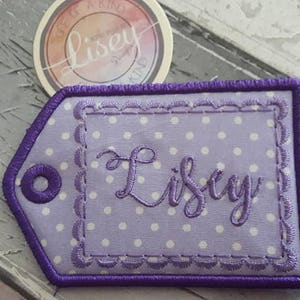 May include: Purple fabric tag with white polka dots and the name "Lisey" embroidered in cursive.