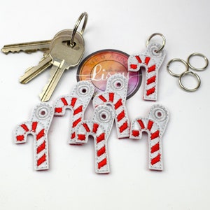 May include: A set of six red and white candy cane keyrings with silver key rings. The keychains are made of felt and are embroidered with red and white stripes.