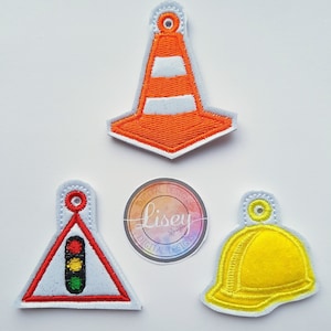 May include: Four felt applique patches with a white background and a glittery texture. The patches are shaped like a traffic cone, a traffic light, a hard hat, and a triangle with a traffic light inside. The patches have a white border and are designed for sewing or iron-on applications.