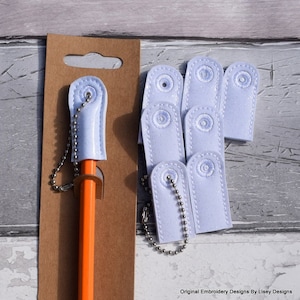 Puede incluir: Un conjunto de diez tapones para lápices blancos con una cadena plateada y un anillo plateado. Los tapones están hechos de un material suave y texturizado y tienen un brillo sutil. Los tapones están empaquetados en un soporte de cartón marrón.