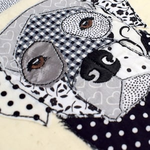 May include: A black and white patchwork fabric dog head with embroidered eyes and nose. The fabric is made of different patterns, including polka dots, gingham, and floral prints.