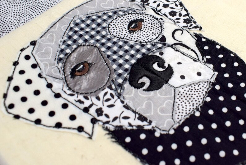 May include: A black and white patchwork fabric dog head with embroidered eyes and nose. The fabric is made of different patterns, including polka dots, gingham, and floral prints.