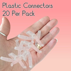 May include: A close-up of a hand holding 20 clear plastic connectors. The connectors are small and have a rectangular shape with a slight curve. The text "Plastic Connectors 20 Per Pack" is visible in the image.