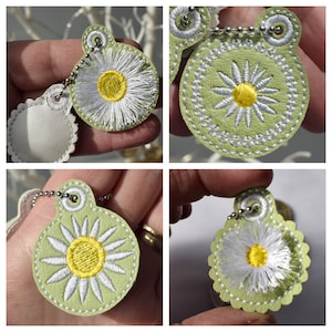 May include: Four green leather keychains with white daisy embroidery. Each keychain has a silver chain and a white circle with a yellow center.