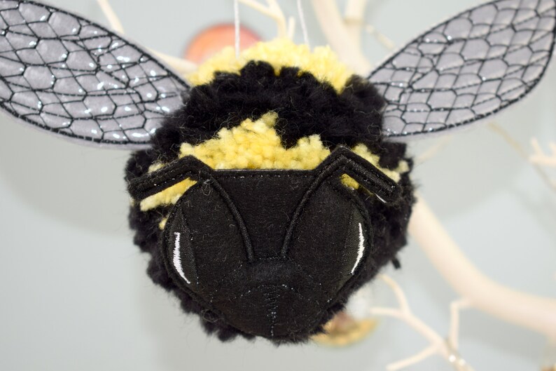 May include: A black and yellow fuzzy bee ornament with black felt wings and a black felt face with white embroidered eyes.