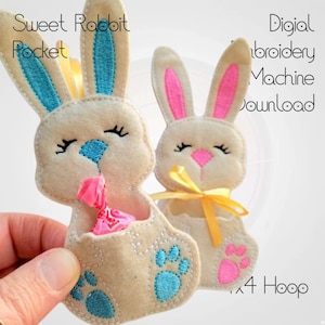 May include: Two felt bunny pocket designs for embroidery machines. The bunny on the left has blue ears and a blue paw print, and the bunny on the right has pink ears and a pink paw print. Both bunnies have a pocket for treats and are designed for a 4x4 hoop.