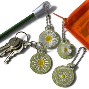 May include: Four green and white daisy keyrings with silver chains. The keyrings are attached to a set of keys and a green pencil with a white eraser.