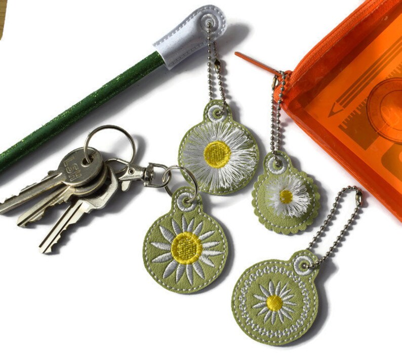 May include: Four green and white daisy keyrings with silver chains. The keyrings are attached to a set of keys and a green pencil with a white eraser.