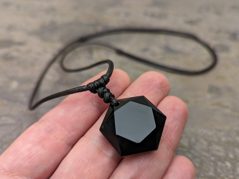 May include: A black obsidian pendant in the shape of a seven-pointed star, hanging from a black cord necklace.