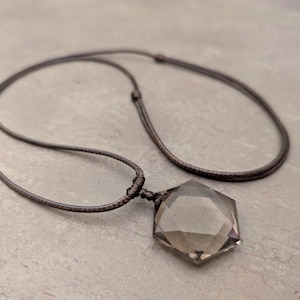 May include: A dark grey gemstone pendant in the shape of a seven-pointed star, hanging from a brown cord necklace.