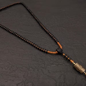 May include: A black and brown wooden bead necklace with a small gold prayer wheel pendant.