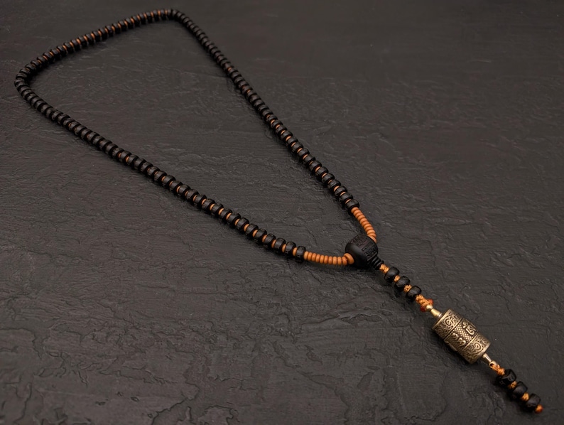 May include: A black and brown wooden bead necklace with a small gold prayer wheel pendant.
