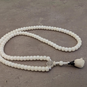 May include: White beaded necklace with a white flower charm and a small metal charm with a geometric design.