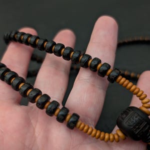 May include: A black and brown beaded necklace with a large black bead at the end. The beads are round and have a smooth texture.