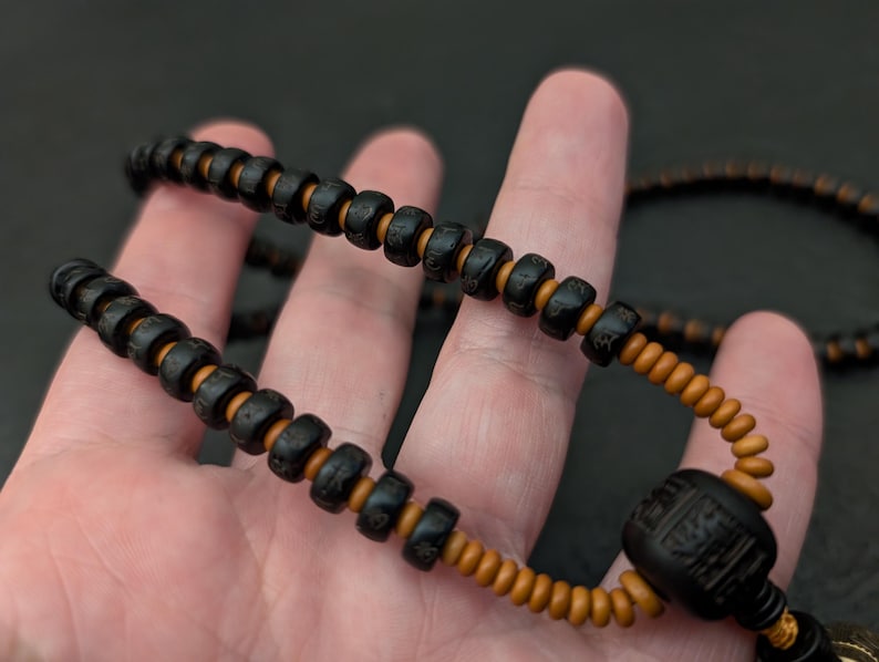 May include: A black and brown beaded necklace with a large black bead at the end. The beads are round and have a smooth texture.