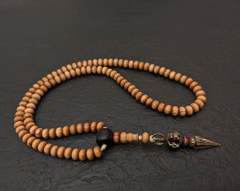 May include: A wooden mala prayer bead necklace with a decorative metal tassel. The beads are brown and have a natural wood grain. The tassel is silver with red and blue accents.