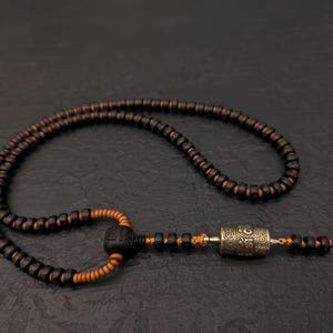May include: A black and brown wooden beaded necklace with a silver prayer wheel pendant.