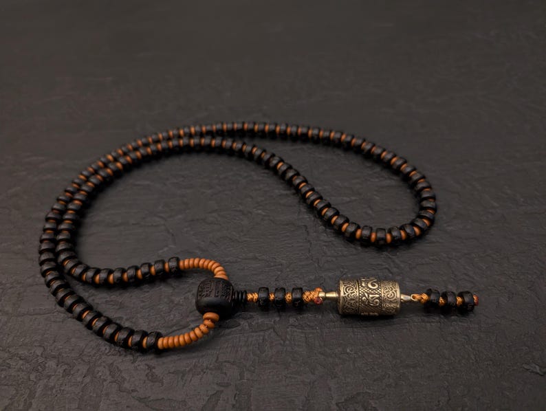 May include: A black and brown wooden beaded necklace with a silver prayer wheel pendant.