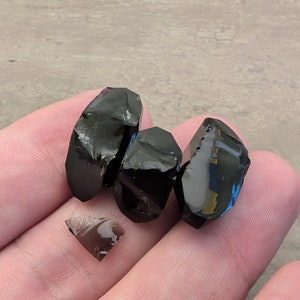 May include: Four pieces of black obsidian, a type of volcanic glass, with a dark, glassy sheen. The pieces are irregularly shaped and have sharp edges.