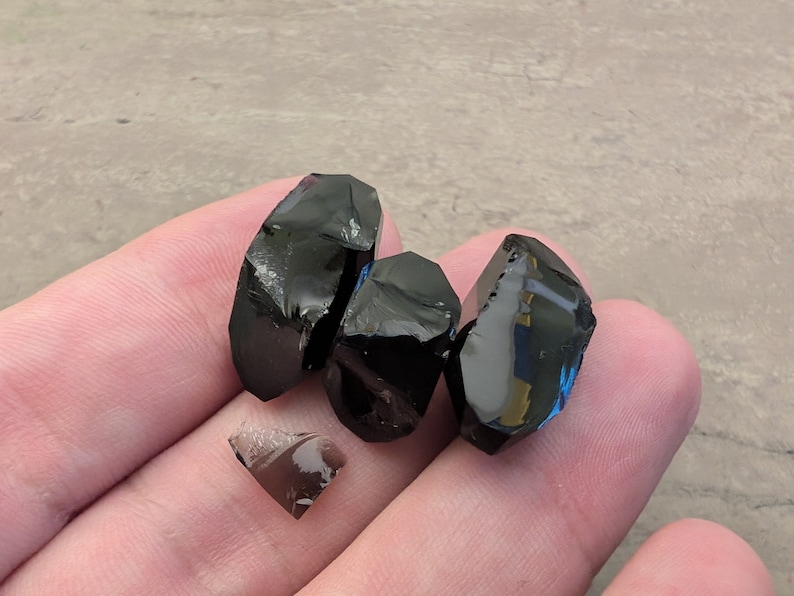 May include: Four pieces of black obsidian, a type of volcanic glass, with a dark, glassy sheen. The pieces are irregularly shaped and have sharp edges.
