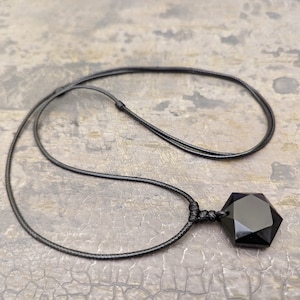 May include: A black obsidian pendant with a seven-pointed star shape hangs from a black cord necklace.