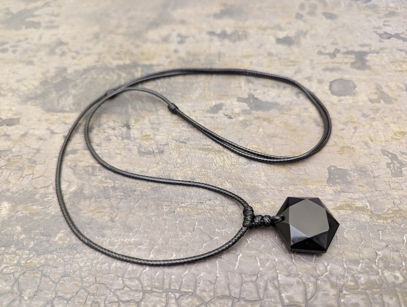 May include: A black obsidian pendant with a seven-pointed star shape hangs from a black cord necklace.