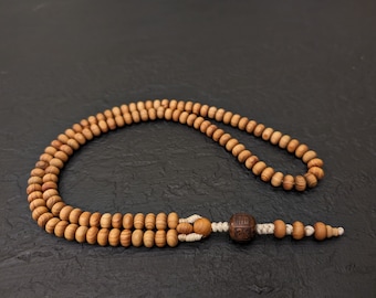 May include: A wooden prayer bead necklace with a brown wooden bead at the end. The beads are light brown and have a natural wood grain.