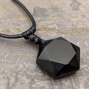 May include: A black onyx pendant in the shape of a seven-pointed star, hanging from a black cord necklace.