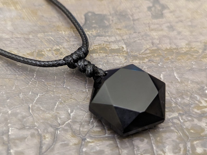 May include: A black onyx pendant in the shape of a seven-pointed star, hanging from a black cord necklace.