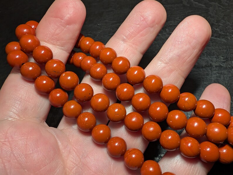 May include: A strand of smooth, round, opaque burnt-orange beads. The beads are uniform in size and shape, featuring a consistent matte to semi-gloss finish with subtle natural variations in the deep orange color throughout the entire string.