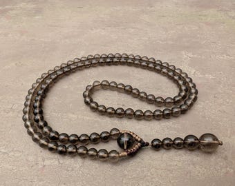 May include: A dark brown beaded necklace with a dark brown tassel. The beads are round and have a smooth, polished finish.