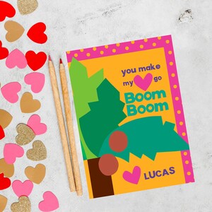 May include: A yellow card with pink polka dots around the edges. The card has a green and brown illustration of a tree with red circles. The text on the card reads "You make my heart go Boom Boom" with a pink heart in the middle. The card is signed "Lucas".
