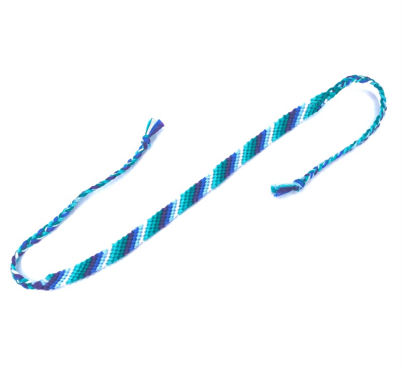 Puede incluir: Un brazalete de amistad azul, verde y blanco con un patr&oacute;n de rayas diagonales.