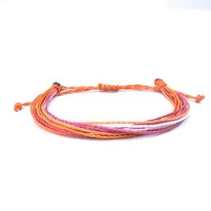 May include: A multi-colored friendship bracelet with orange, pink, and white threads. The bracelet is tied with a knot at the end.