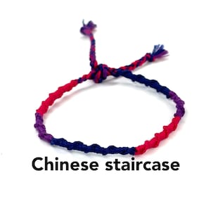 May include: A colorful friendship bracelet made with pink, blue, and purple thread. The bracelet is tied in a "Chinese staircase" knot.