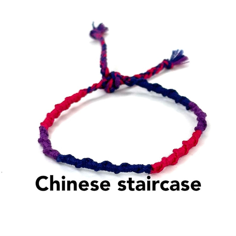 May include: A colorful friendship bracelet made with pink, blue, and purple thread. The bracelet is tied in a "Chinese staircase" knot.