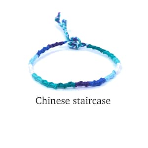 Puede incluir: Un brazalete de amistad trenzado azul, verde, morado y blanco con un nudo en el extremo. El brazalete se llama "escalera china".